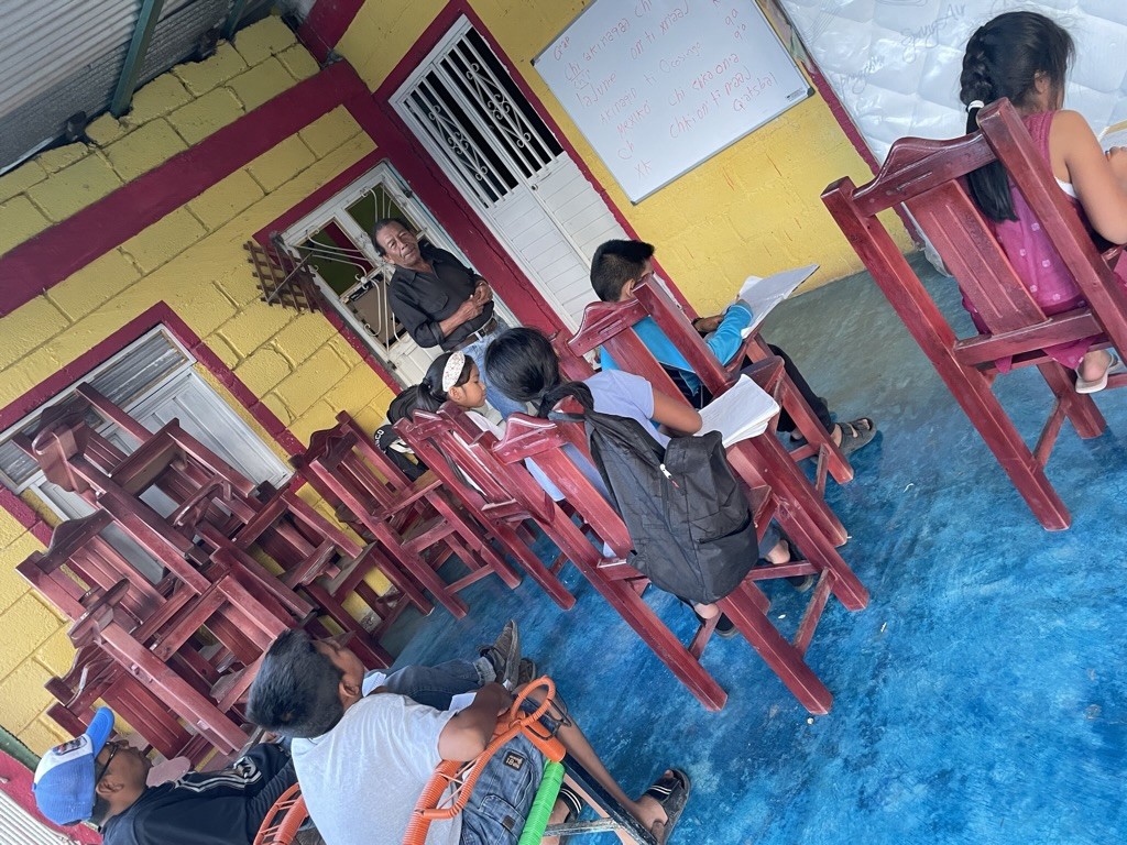 Teodoso Ortíz Ramírez teaching Moocho' (Mayan language) to four children and one adult.