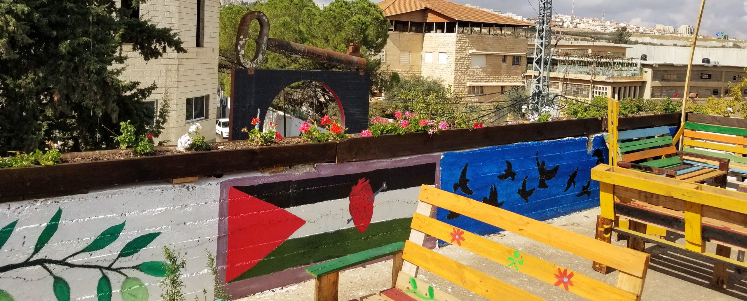 Rooftop setting with painted Palestinian flag, flowers, and key of return monument.