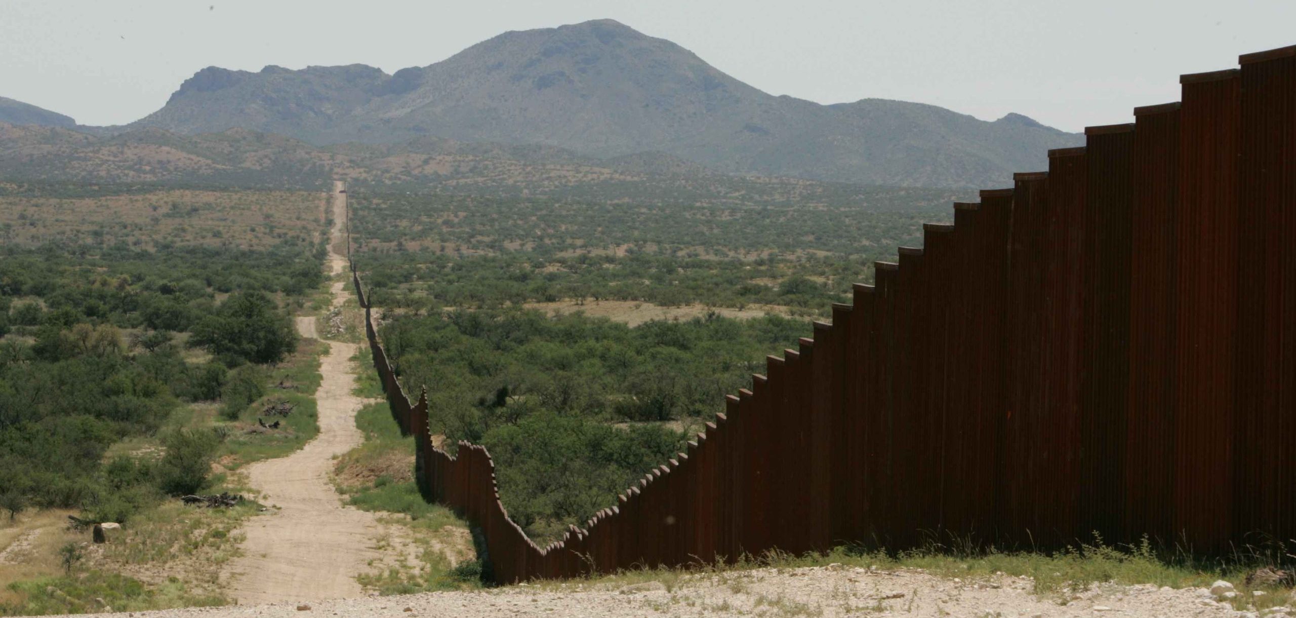 A rusted metal fence stretches across a desolate landscape separating Mexico from the U.S.